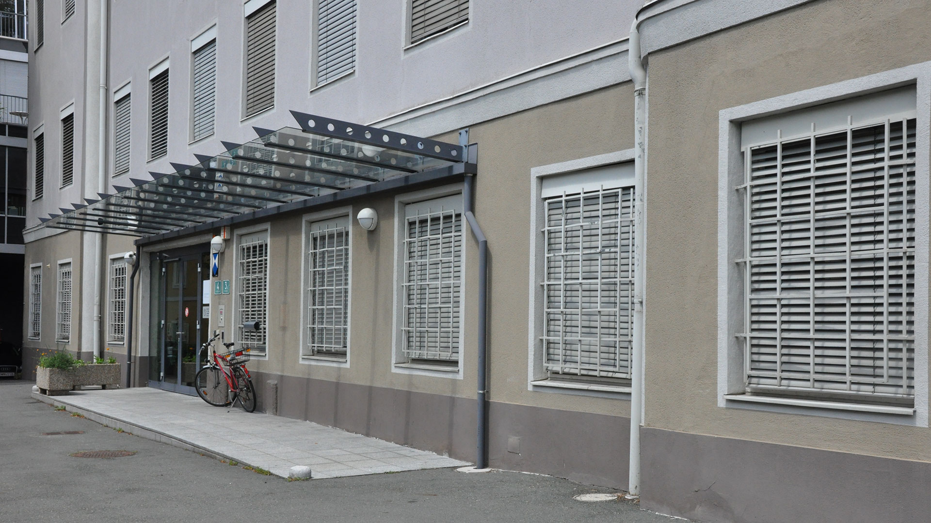 An einer braucnen Häuserfront ist der überdachte Eingang des Stadtarchives Graz zu sehen. Vor dem Eingang ist ein Fahrrad geparkt.