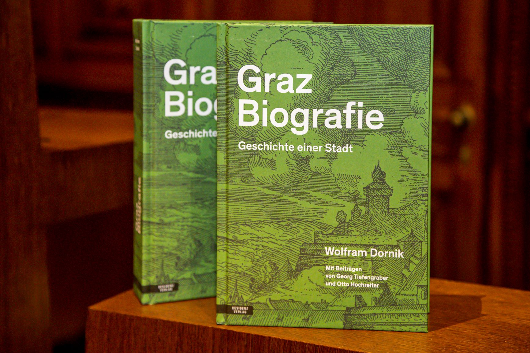 Auf einem dunkelbraunen Holzpult sind zwei Exemplare des Buches Graz Biografie nebeneinander aufgestellt.