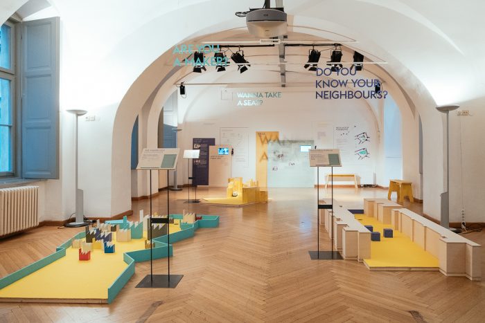 Ausstellungsraum mit interaktiven Displays, farbenfrohen geometrischen Installationen und Einblicken in die Stadtgestaltung.