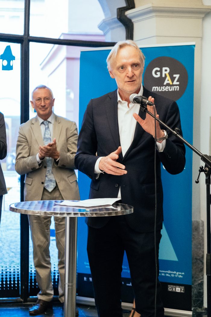 Ein Mann im Anzug spricht auf einem Podium über Stadtgestaltung vor einem Banner des Graz Museums.