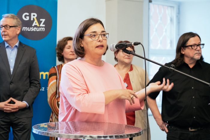 Eine Frau spricht vor einer Gruppe im Graz Museum an einem Mikrofon über Stadtgestaltung.