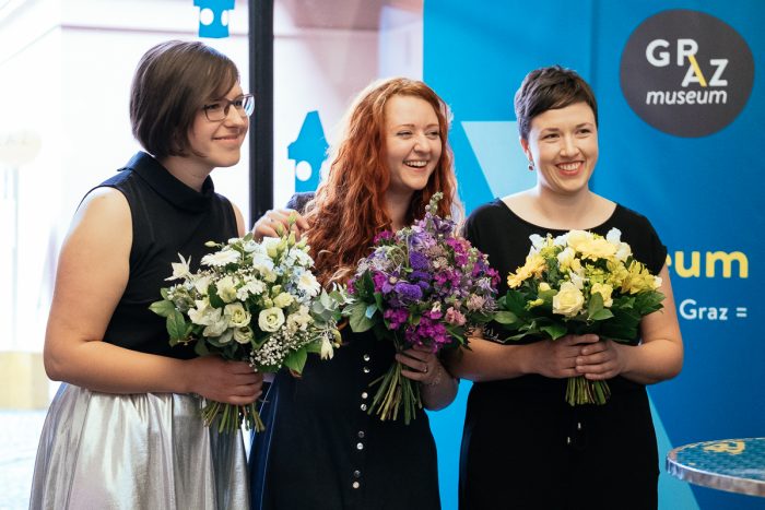 Drei Frauen mit Blumensträußen stehen bei einer Human Cities-Veranstaltung im Graz Museum zusammen.