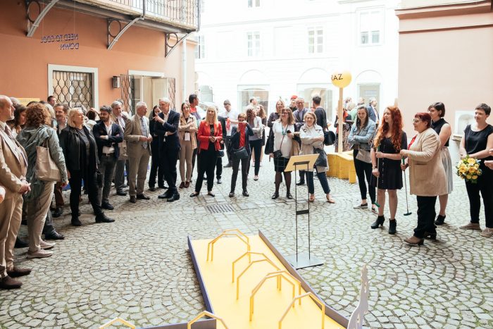 Eine Gruppe versammelt sich in einem Innenhof und diskutiert über Stadtplanung, während sie einem Redner auf einem Podium zuhört.