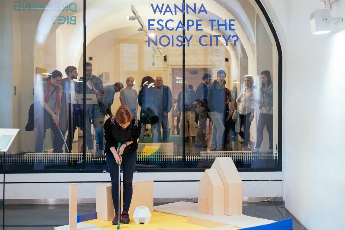 Eine Frau erkundet eine Ausstellung über menschliche Städte, während andere über Lösungen für die Stadtgestaltung nachdenken.