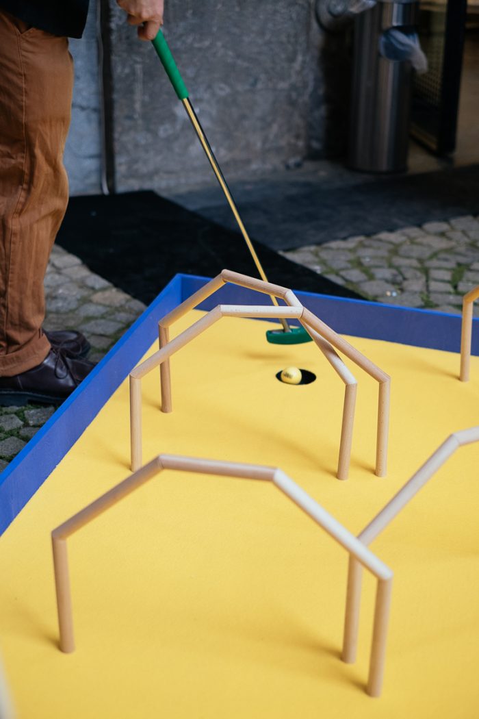 Eine Person spielt Minigolf auf einem gelben Platz und genießt die vom Urban Design inspirierten Holzbögen.