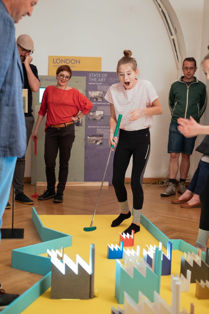 Eine junge Frau spielt Indoor-Minigolf und formt in einem hell erleuchteten Raum menschliche Städte durch Spaß.