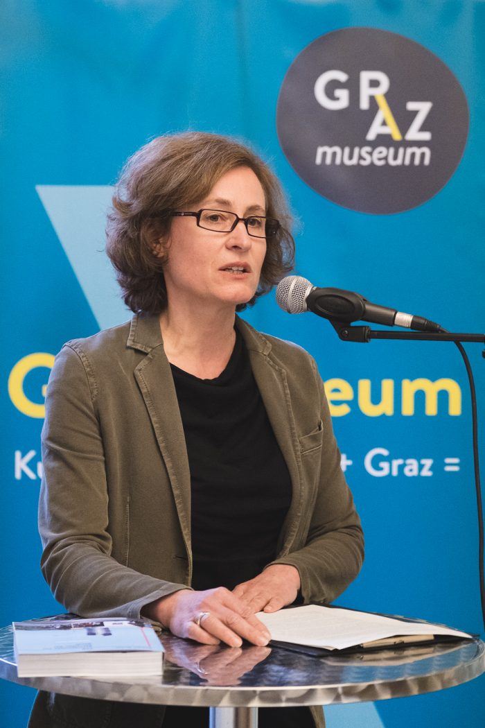 Eine Frau spricht an einem Podium mit Mikrofon im Graz Museum.
