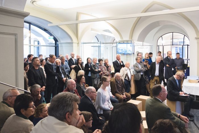 Eine Gruppe von Personen besucht eine Präsentation oder einen Vortrag in einem modernen Innenraum.