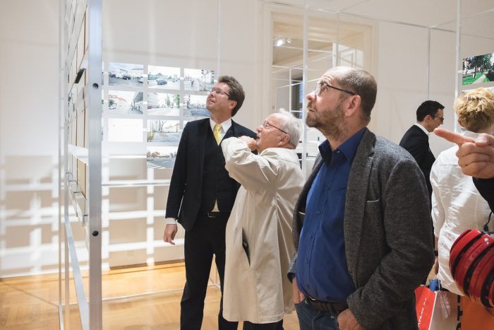 Drei Männer betrachten die Displays an einer weißen Wand in einem gut beleuchteten Ausstellungsraum.