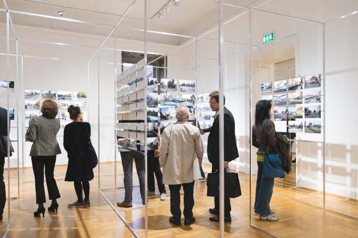 Betrachter von Fotografien, die auf Drahtgittertafeln in einer modernen Kunstgalerie ausgestellt sind.