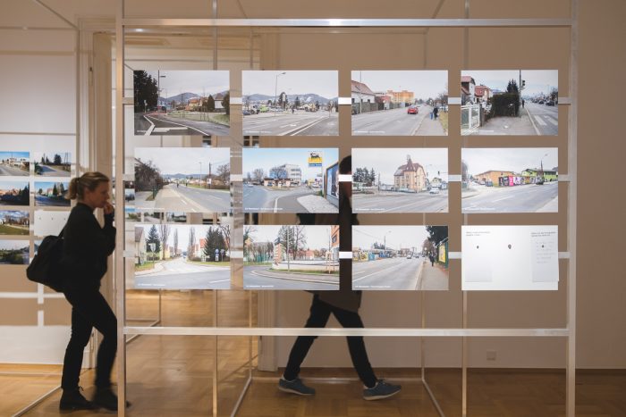 Zwei Personen gehen an einer Ausstellung von Straßenfotografien auf Tafeln in einer Kunstgalerie vorbei.