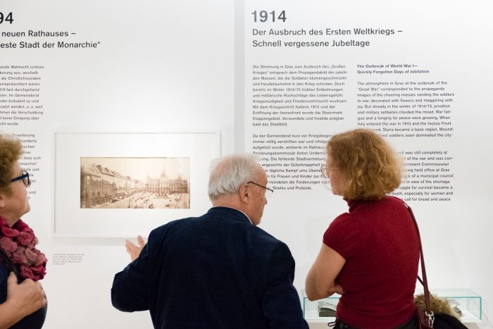 Drei Personen betrachten ein Exponat und ein Foto der Republik 1918-1938 in einem Museum in Graz.