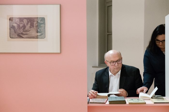 Zwei Personen sitzen in Graz an einem rosa Schreibtisch und lesen Bücher unter gerahmter Kunst der Republik 1918-1938.