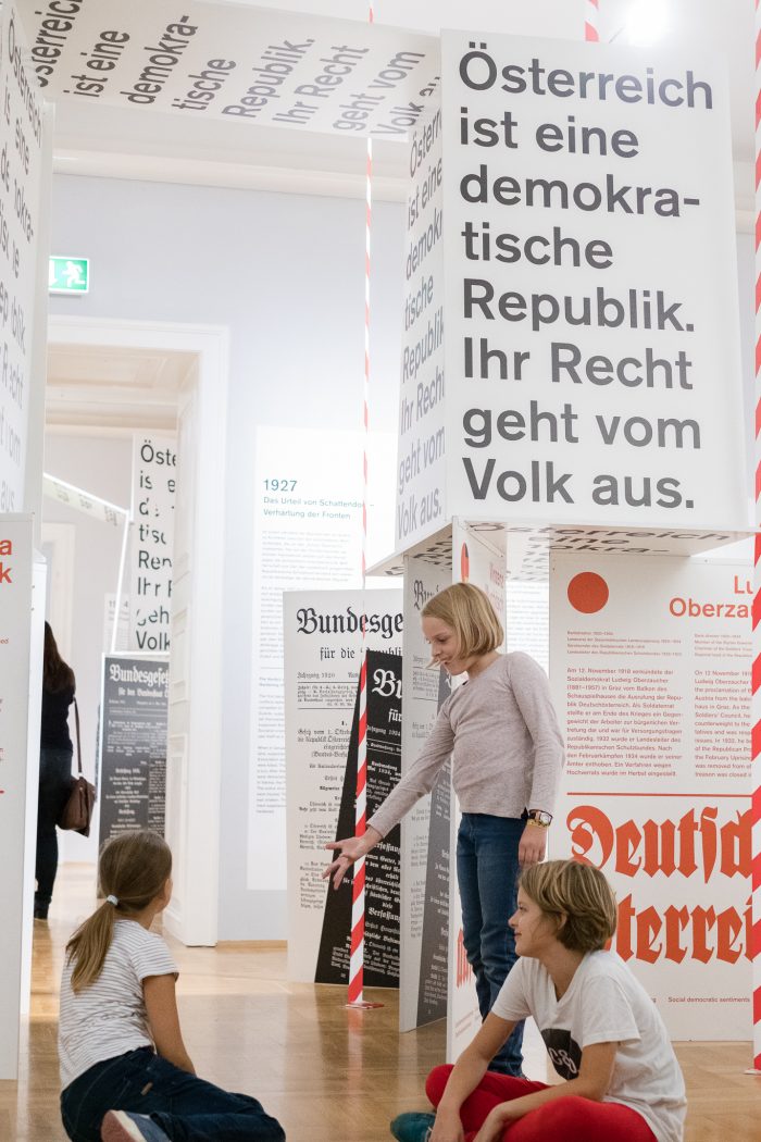 Drei Kinder erkunden die Ausstellung im Grazer Kartenhaus der Republik unter den Tafeln von 1918-1938.