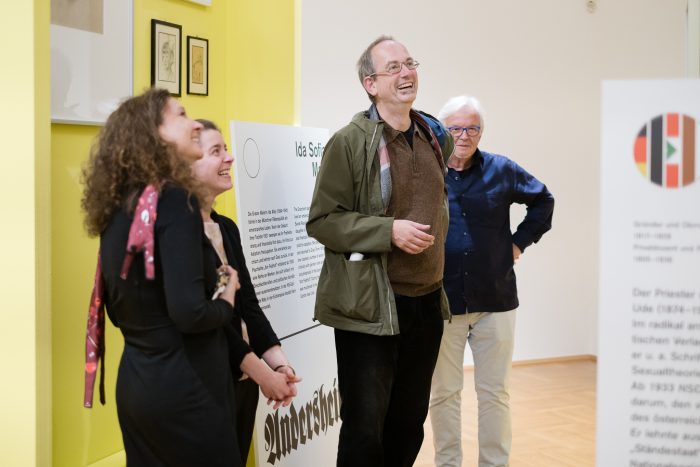 Vier Erwachsene lächeln zusammen in einer modernen Kunstgalerie in Graz.