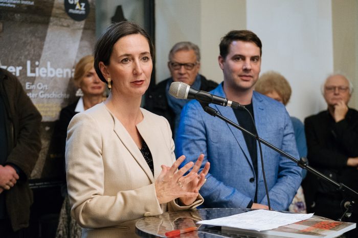 Eine Frau spricht an einem Podium über das Lager Liebenau, während andere im Hintergrund stehen.