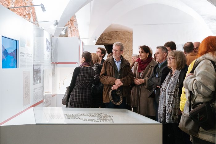 Eine Gruppe betrachtet die Exponate und die Informationstafeln des Lagers Liebenau in einer Museumsumgebung.