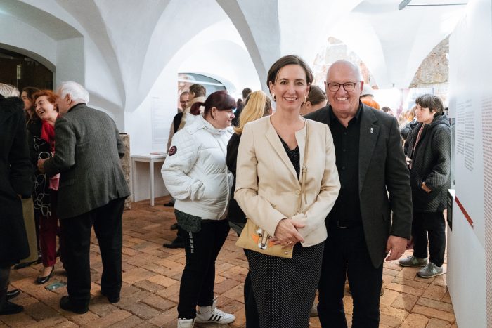 Eine Gruppe bei einer Indoor-Veranstaltung im Lager Liebenau, mit zwei lächelnden Personen im Vordergrund.