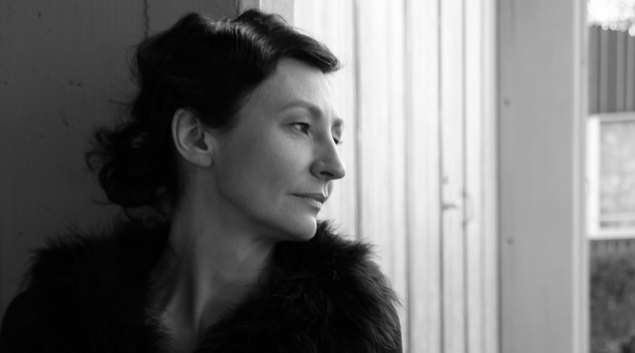 Frau mit kurzen dunklen Haaren, ein Hitlermädel, schaut aus einem Fenster in Schwarz-Weiß-Foto.