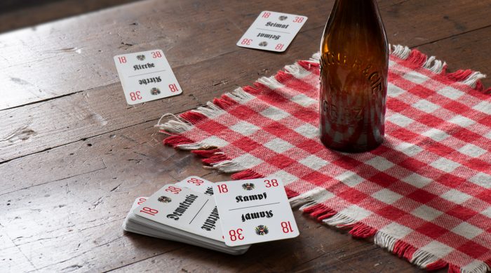 Spielkarten erinnern an Graz 1918 - 1938 auf einem rot karierten Tuch auf einem Holztisch.