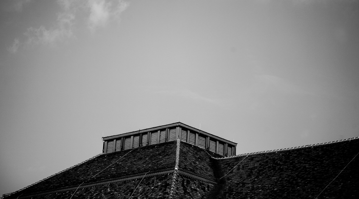 Schwarz-Weiß-Foto eines überdachten Schauplatzes mit einem quadratischen Schlot gegen einen klaren Himmel.