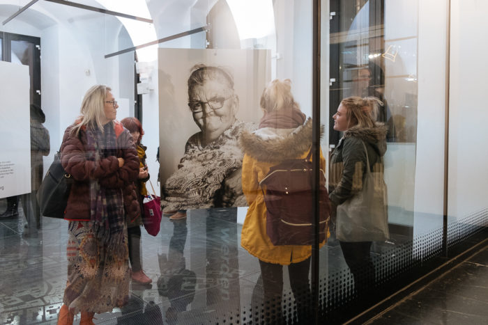 Vier Frauen betrachten ein großes Schwarz-Weiß-Porträt in einer Kunstgalerie durch eine Glaswand.