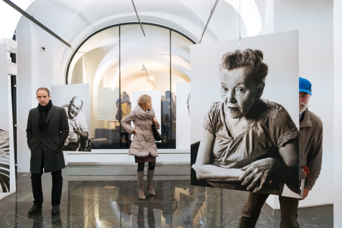 In einer modernen Kunstgalerie mit gewölbten weißen Wänden werden große Schwarz-Weiß-Porträts betrachtet.