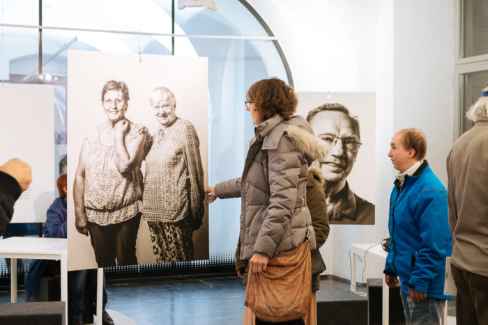 Menschen betrachten große Schwarz-Weiß-Porträts in einer Indoor-Kunstausstellung.