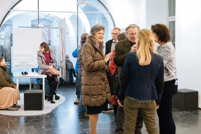 Menschen, die sich in einer modernen Kunstgalerie mit weißen Wänden und schwarzem Fußboden unterhalten und beobachten.