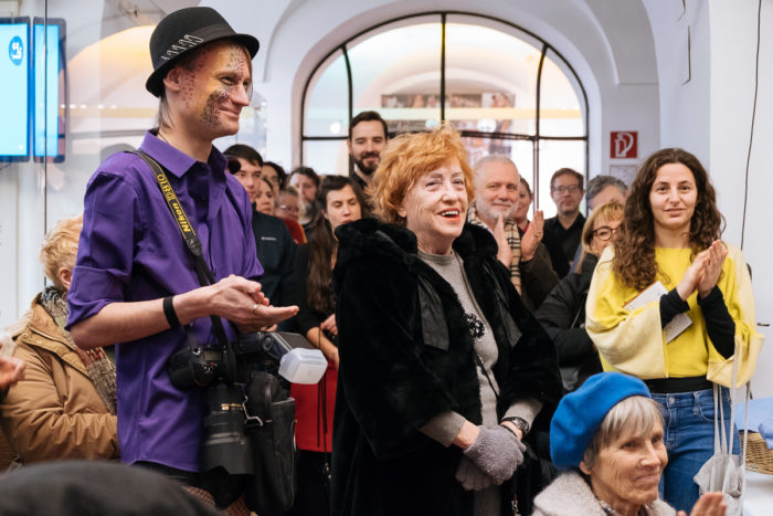Eine Gruppe von Menschen steht in einem Haus, ganz normal anders, klatscht und lächelt über ein unsichtbares Ereignis.