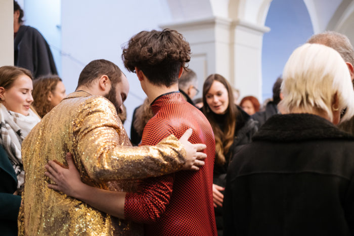 Zwei Menschen umarmen sich in einer überfüllten Halle - ganz normal anders, aber tief verbunden.