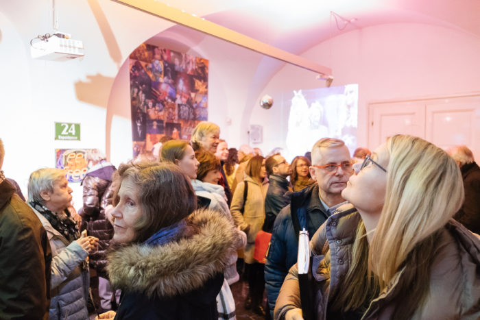 Ein ganz normales anderes Publikum in Winterkleidung versammelt sich drinnen inmitten einer bunten Veranstaltungsbeleuchtung.