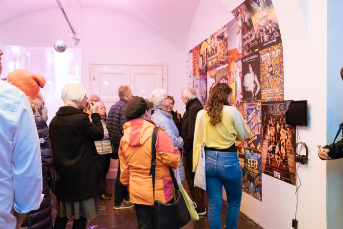 Eine Gruppe von Menschen betrachtet ganz normal andere Plakate und Displays in einem hell erleuchteten Innenraum.