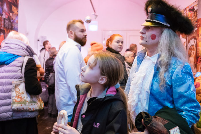 Ein ganz normales anderes Publikum in einem hellen Raum; Mann im Kostüm, Mädchen mit Sandwich vorne.