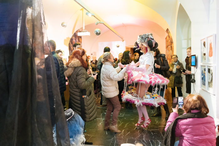 Die Menge schaut zu, wie eine ganz normale Person in einem rosa-weißen Kostüm mit einem Gast in einem Haus tanzt.