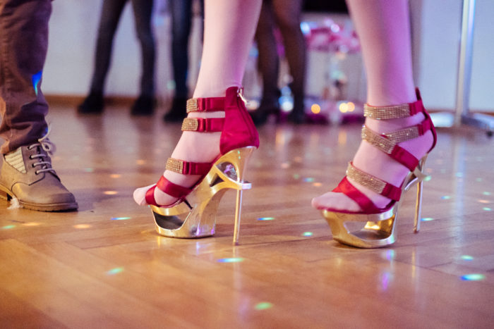 Person in goldenen und roten Stöckelschuhen auf einem Holzboden - ganz normal anders mit lebhaften Reflexen.