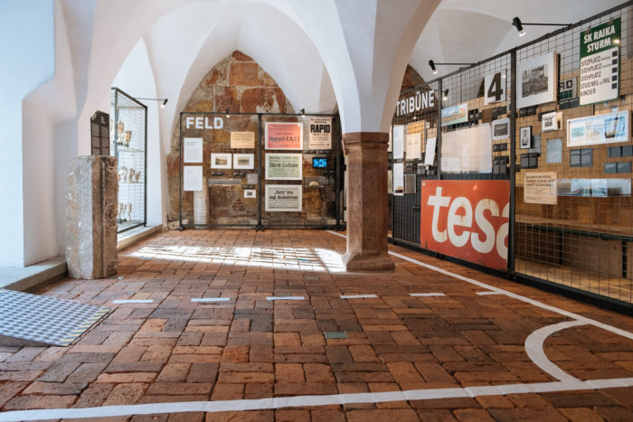 Museumsexponat mit Backsteinboden, Steinsäulen und Sturm-Themen auf Drahttafeln.