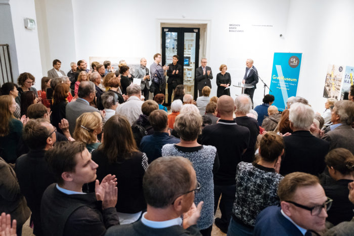Ein Publikum hört einem Redner bei einer feierlichen Bäder-Veranstaltung in einem Museum oder einer Galerie zu.
