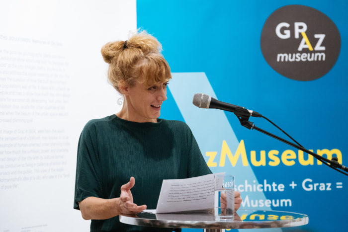 Eine Frau spricht an einem Podium mit Notizen in der Hand im Graz Museum.