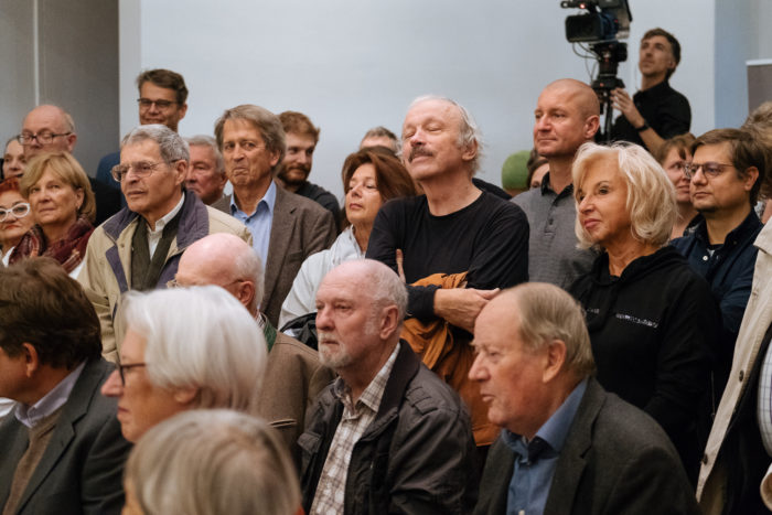 Eine Gruppe Erwachsener hört bei einer Brückenveranstaltung oder -präsentation aufmerksam zu.