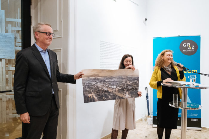 Drei Personen präsentieren bei einer Museumsveranstaltung einen alten Stadtplan, auf dem alte Boulevards markiert sind.