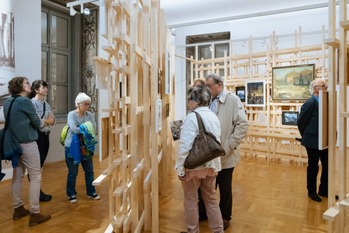 Eine Gruppe bewundert Gemälde von Boulevards, die auf Holzrahmen in einer Kunstgalerie ausgestellt sind.