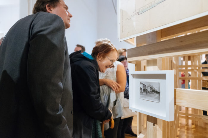 Menschen, die gerahmte Fotos und Dokumente in einer überdachten Brücken- oder Boulevard-Galerie betrachten.