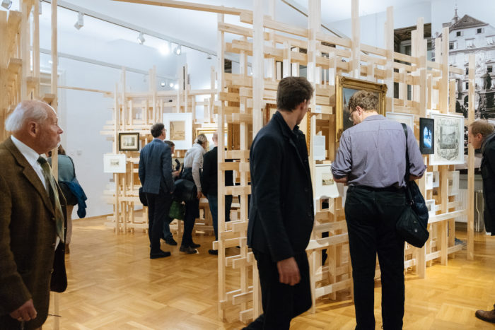 Menschen betrachten Kunstwerke auf Holzkonstruktionen in einer modernen Galerie mit Boulevards in der Nähe.