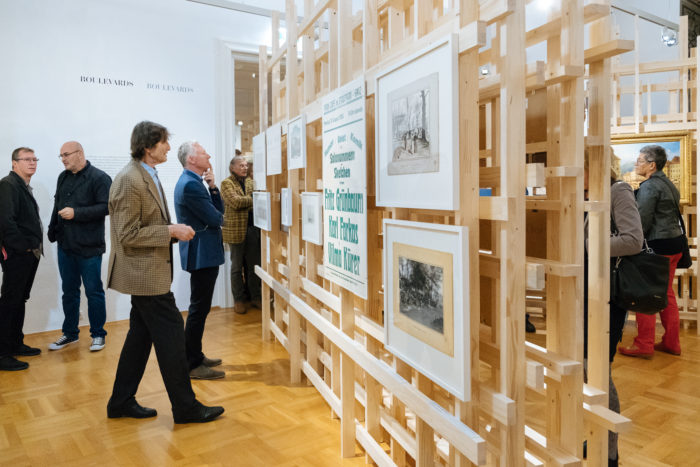 In einer Galerie mit hellen Holzfußböden und Boulevards können die Besucher Kunstwerke auf Holzkonstruktionen betrachten.