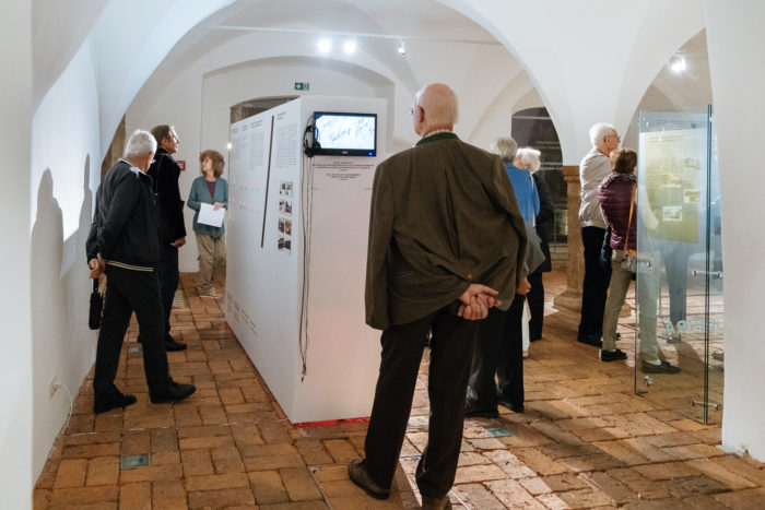 In einer Kunstgalerie mit Backsteinböden und Gewölbedecken betrachten die Besucher die ausgestellten Werke und Exponate.
