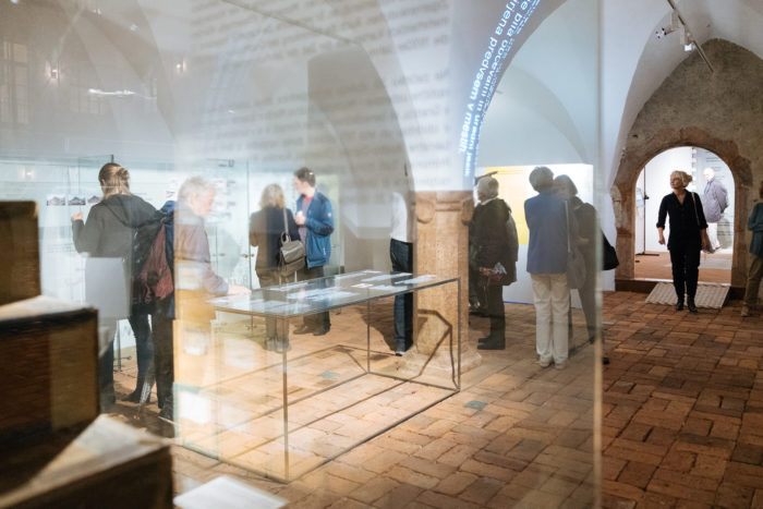 Menschen, die Exponate in einem Museum mit Glasvitrinen und gewölbten Decken betrachten.