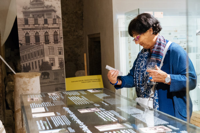 Eine Frau liest eine Karte, während sie vor einem Ausstellungsstück steht und in der anderen Hand ein Glas hält.