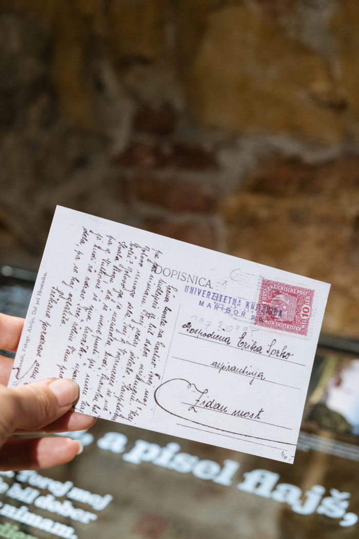 Eine Hand hält eine handgeschriebene Postkarte mit einer roten Briefmarke und polnischem Text.