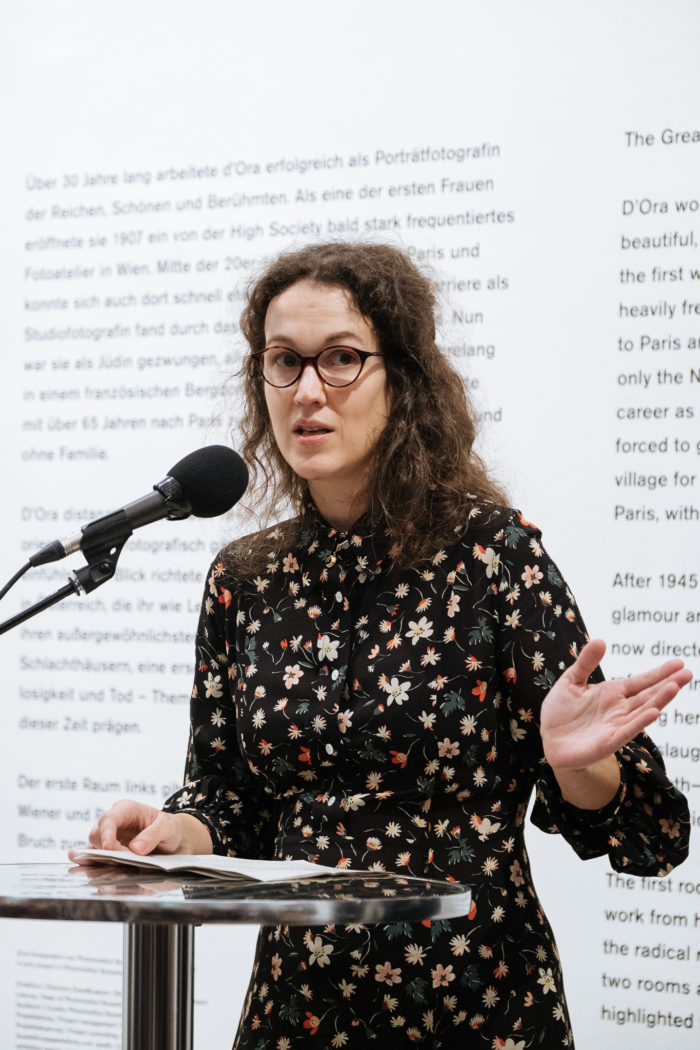 Eine Frau mit Brille spricht auf einem Podium über den großen Bruch und gestikuliert mit einer Hand.